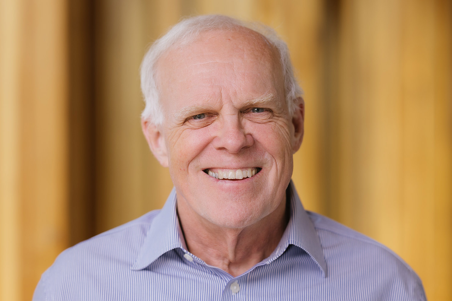 Portrait of John Hennessy smiling, in a blue striped shirt.