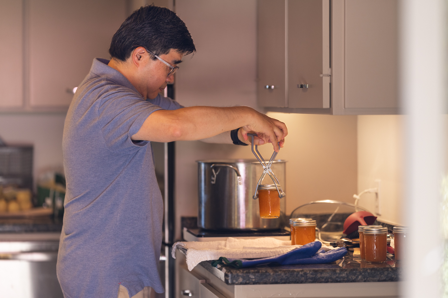 Man using jar tongs to lift a hot jar of apricot jam from a canning pot.
