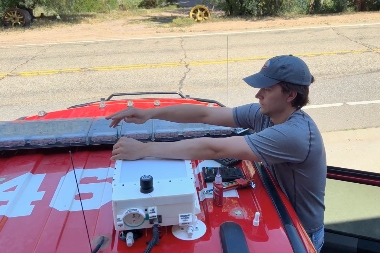 Open video Man in cap installs a white sensor box on the roof of a red fire engine. in a modal