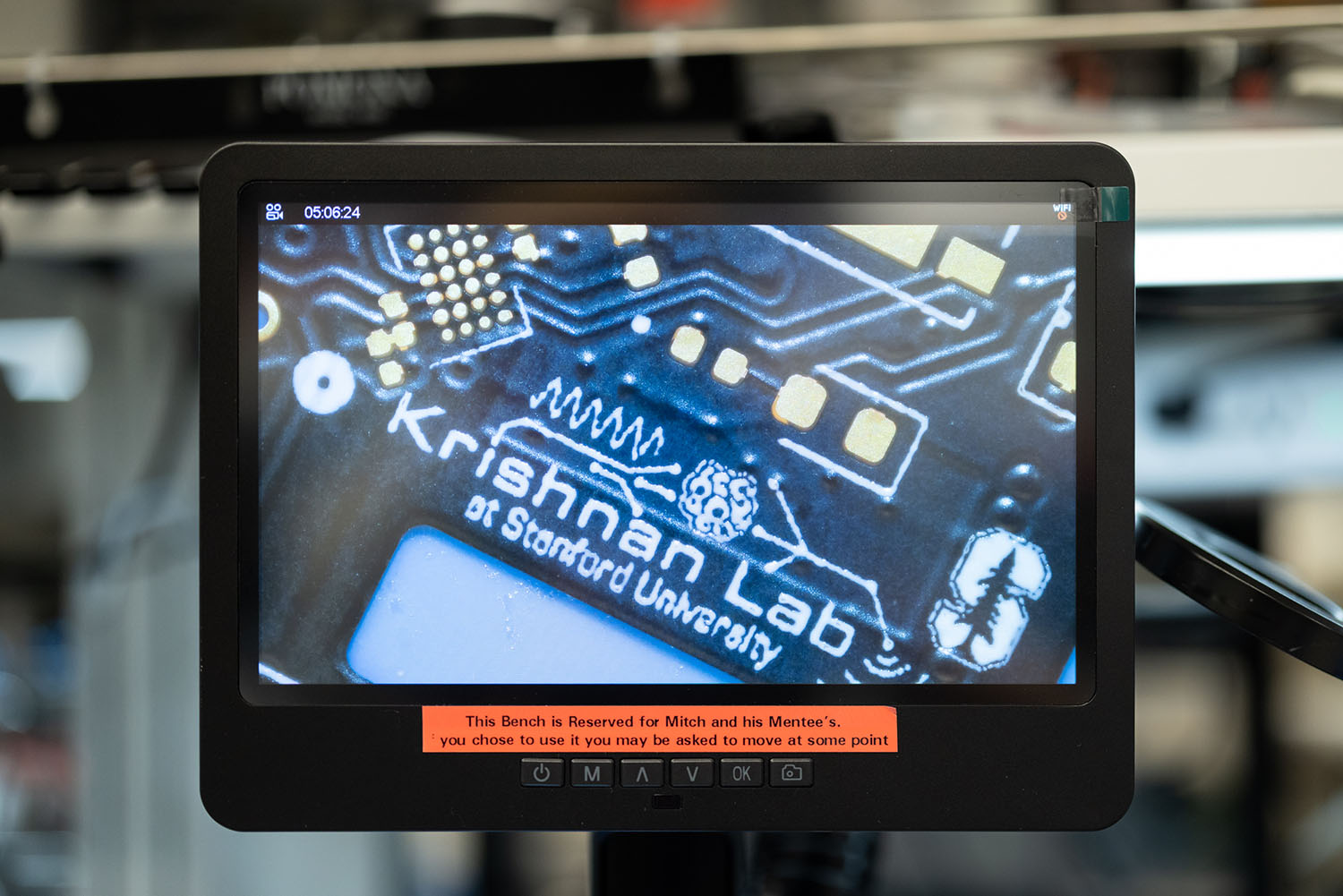 A digital microscope screen shows a magnified circuit board labeled "Krishnan Lab at Stanford University" with a Stanford tree logo.