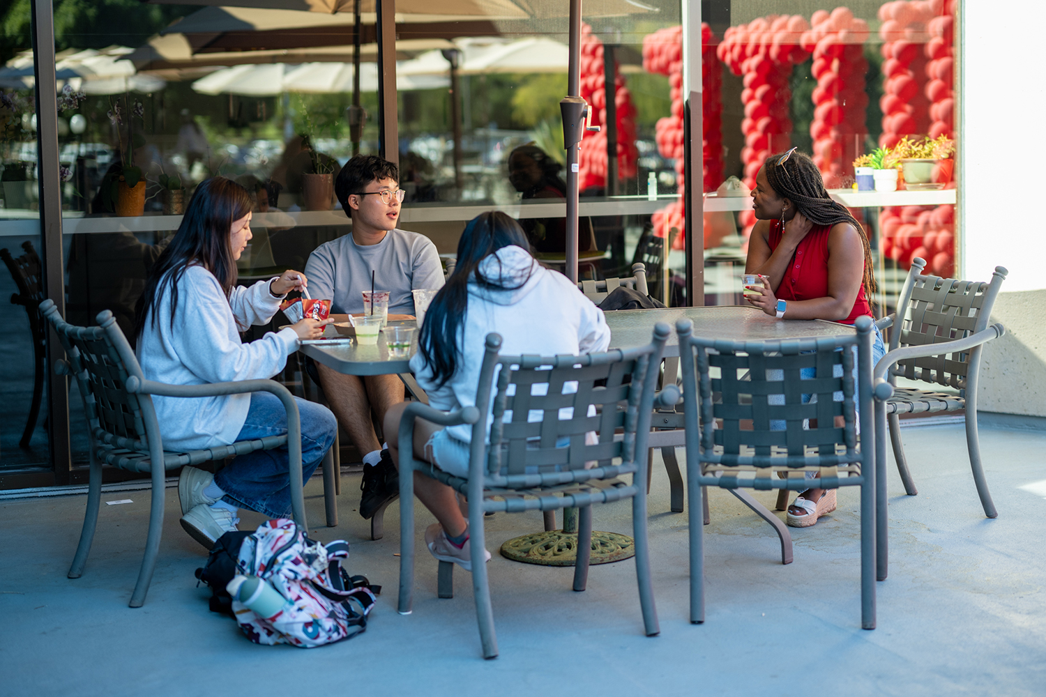 Four students sit around an outdoor table, chatting while enjoying drinks and snacks.