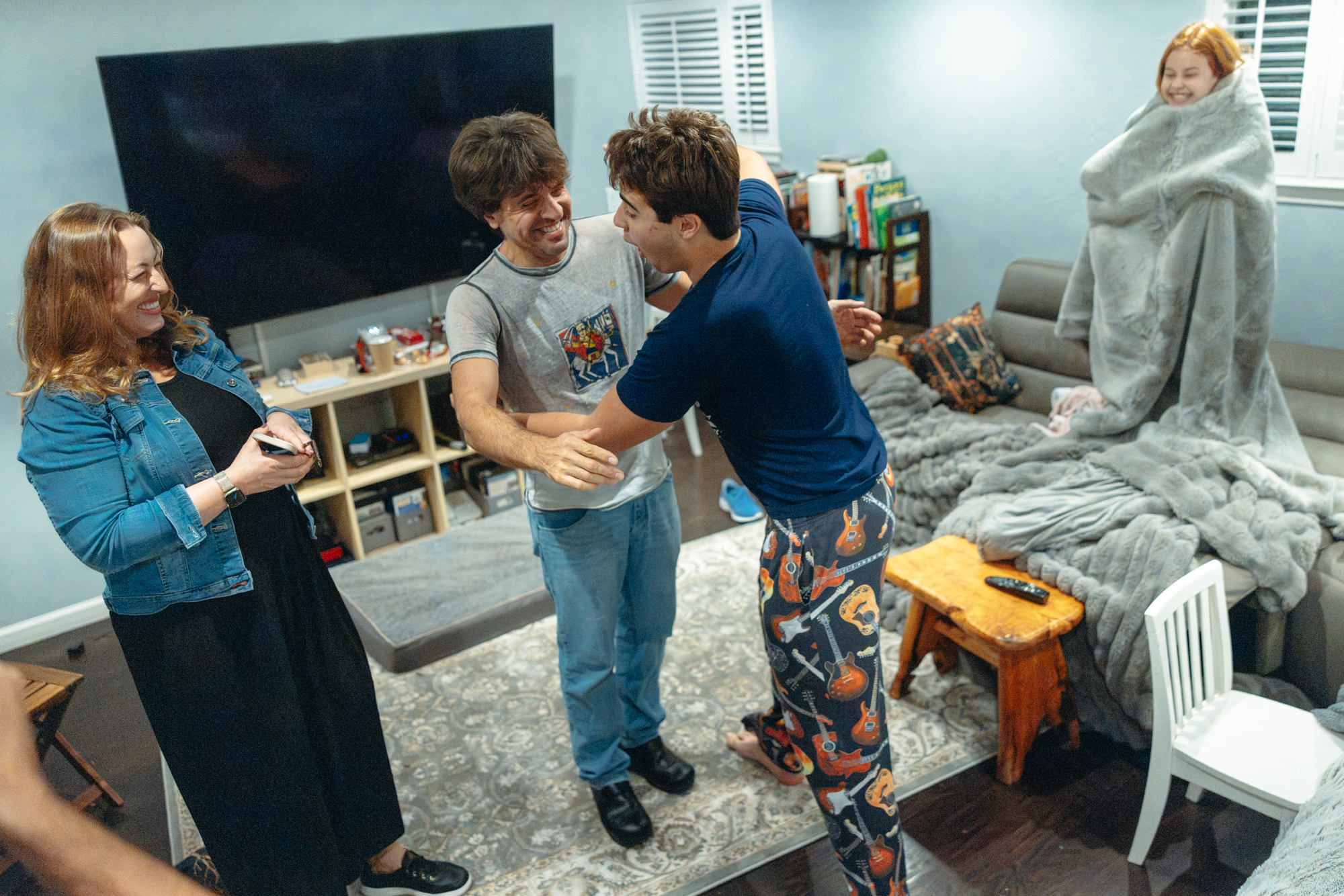 Karl Deisseroth and son Hudson in guitar-print pajama pants embrace excitedly as mom and sister laugh.