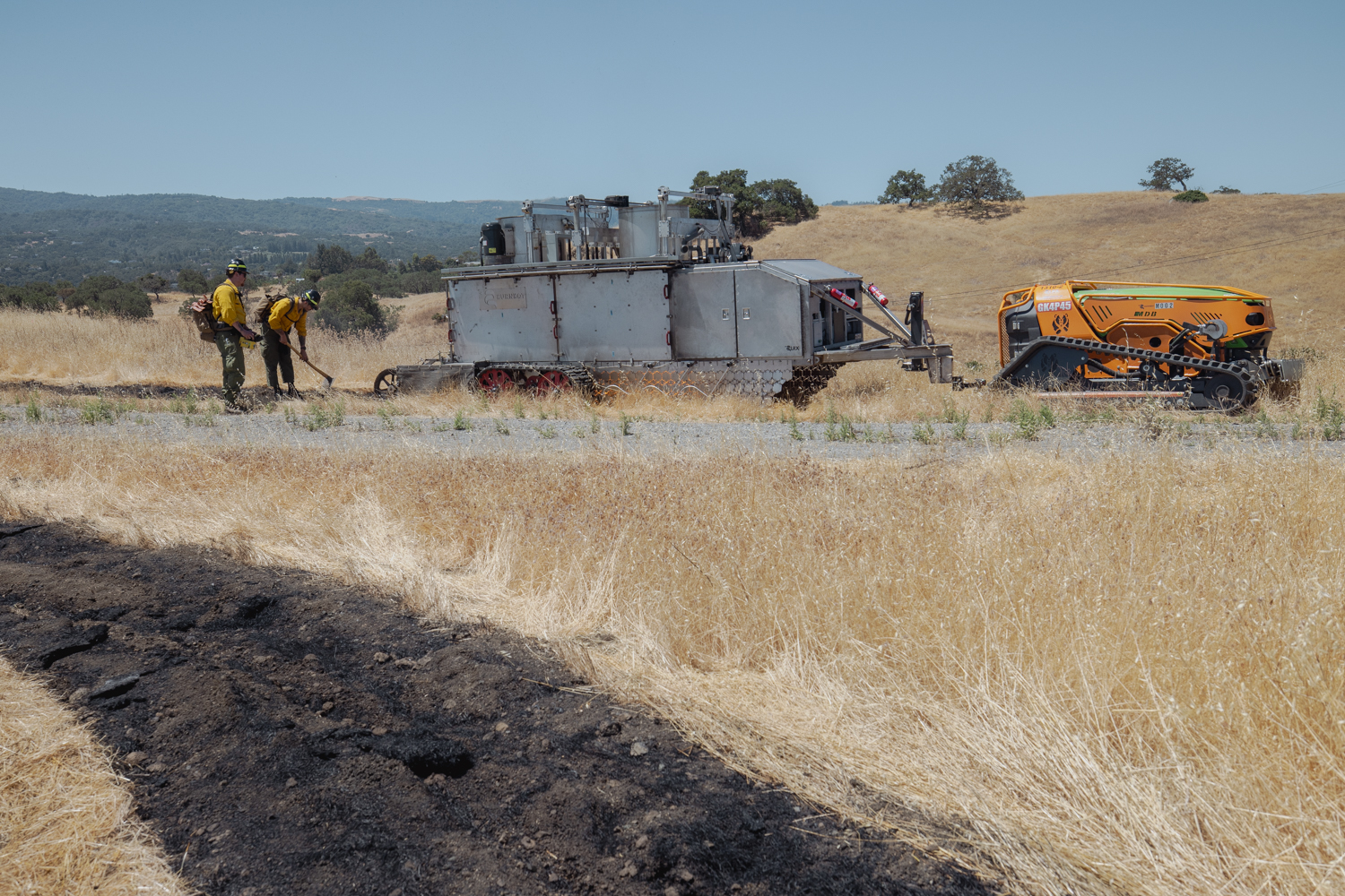 A scorched path of earth frames the large BurnBot machine, which is pulled by a small tractor-like vehicle.