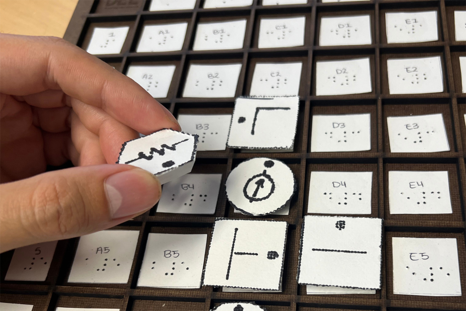 Hand holding tactile engineering symbol in front of Braille-labeled grid.