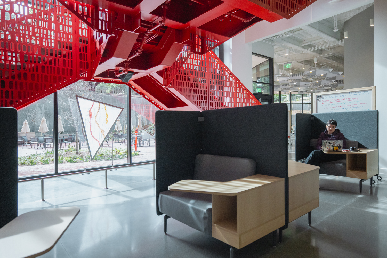 View of study seating on the first floor, with red staircase, art, and outdoor patio seating in background.