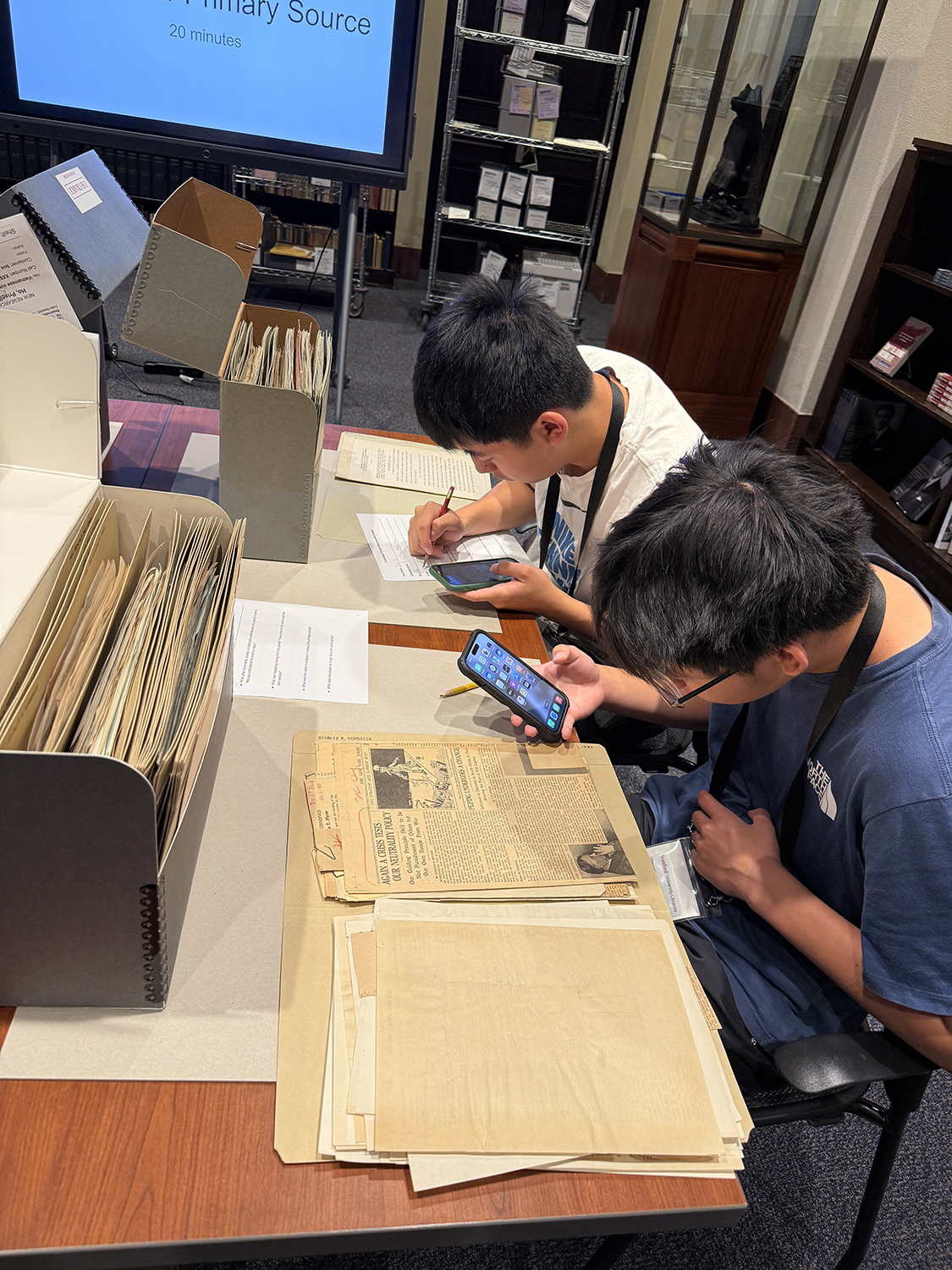 Image of two students interacting with primary sources including historical newspaper clippings.