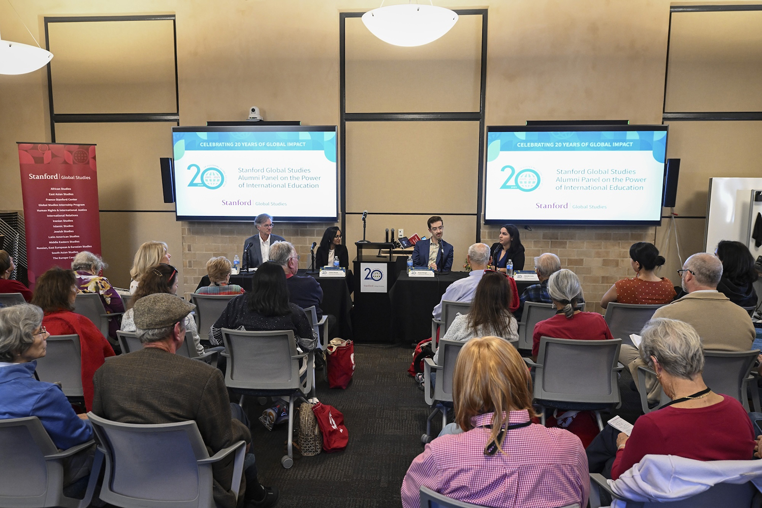 An alumni panel event with speakers at a table in front of an audience, celebrating 20 years of global impact in education.