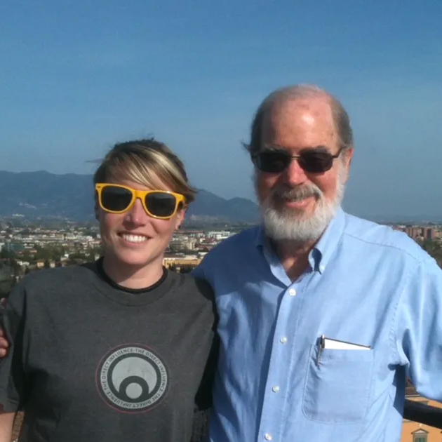 Two people stand together outdoors with a cityscape and mountains in the background, sharing a moment of connection.