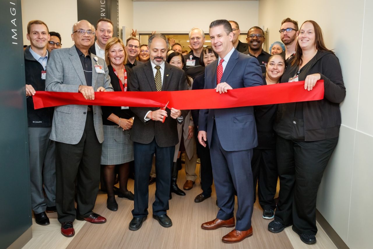 Group of people gather for a ribbon-cutting ceremony, celebrating the opening of new hospital with a large red ribbon.