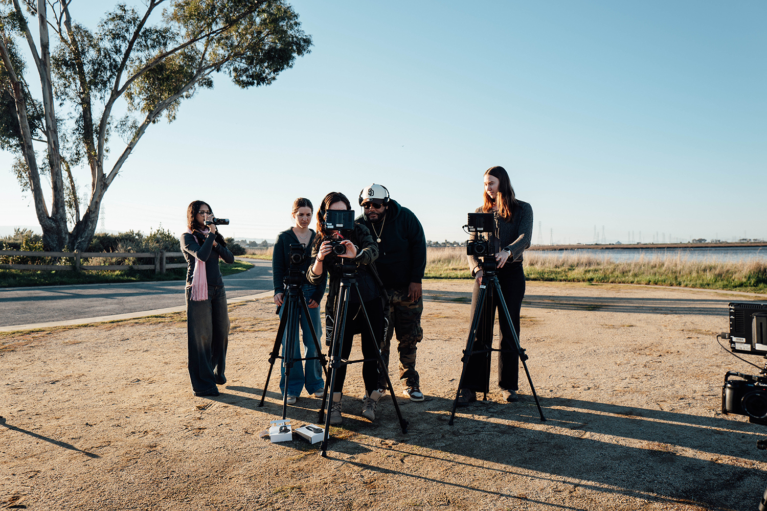 A group of five individuals set up cameras on tripods in an outdoor area, preparing for a video shoot.