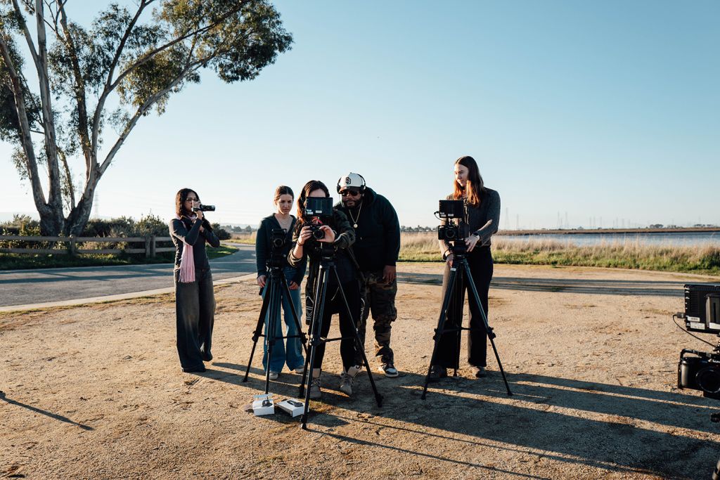 A group of five individuals set up cameras on tripods in an outdoor area, preparing for a video shoot.