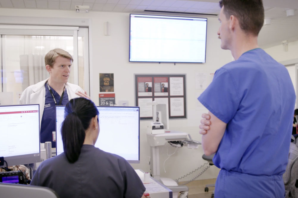 Open video Healthcare professionals in discussion in a hospital setting with computers and screens. in a modal