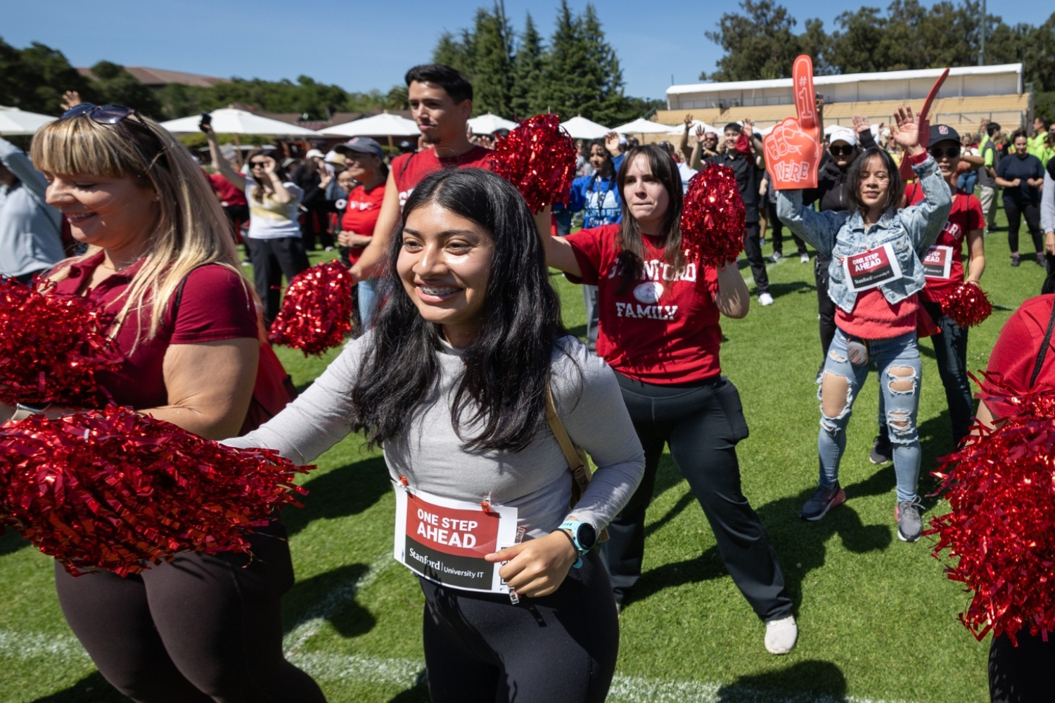 A lively crowd cheers and waves pom-poms during a community event, showcasing enthusiasm and spirit on a sunny day.