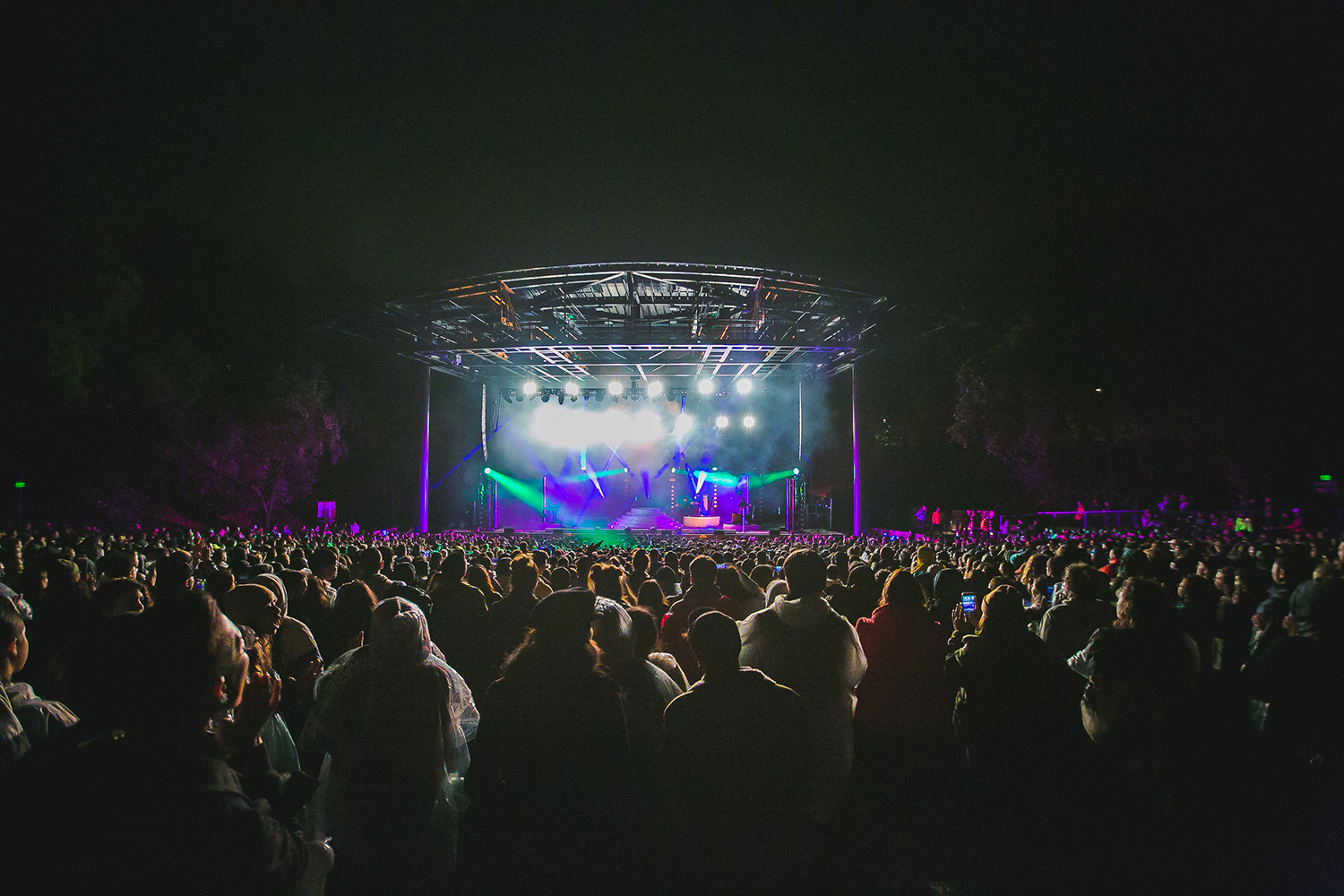 A crowd gathered at an outdoor concert under colorful lights, with a stage set up for a Kali Uchis concert at night.