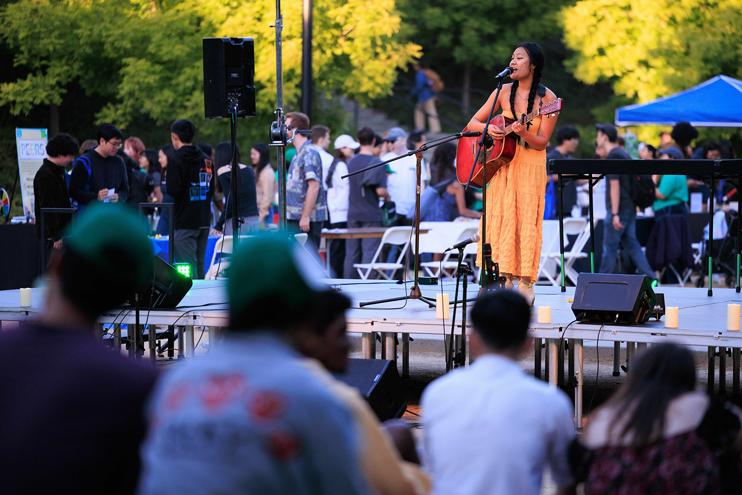 A musician performs on stage with a guitar at an outdoor event, while the audience enjoys the show.