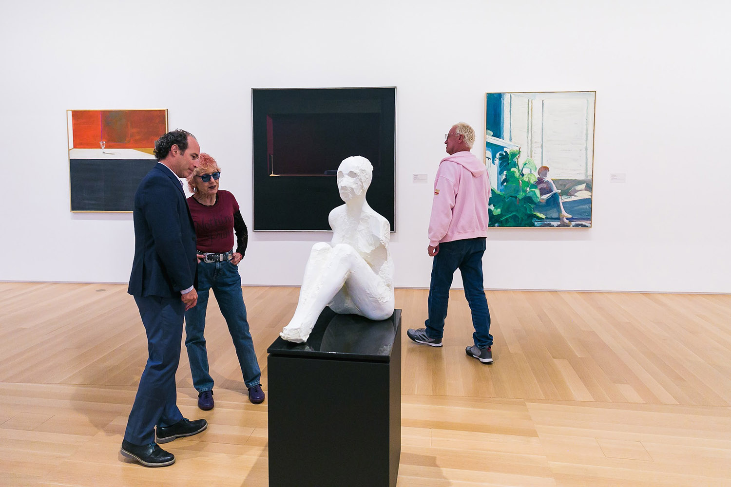 Linetzky and artist Judy Chicago stand near a white sculpture of a nude torso and colorful paintings in an art gallery.