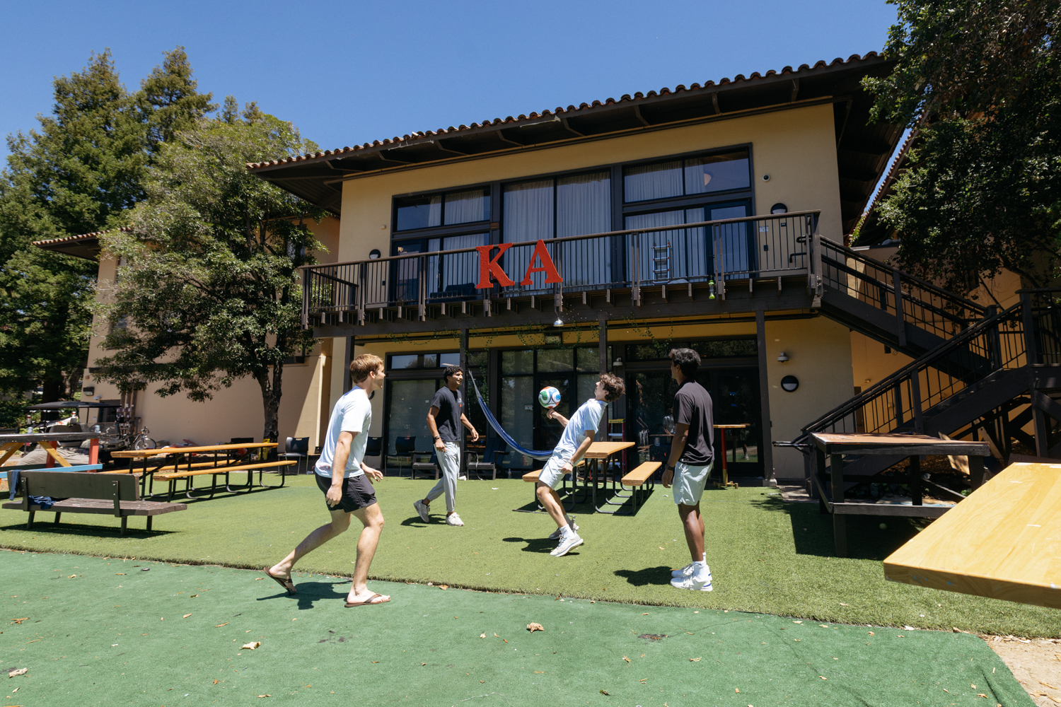 Samir Banerjee and three friends kick a soccer ball on the lawn outside a campus house on a sunny day.
