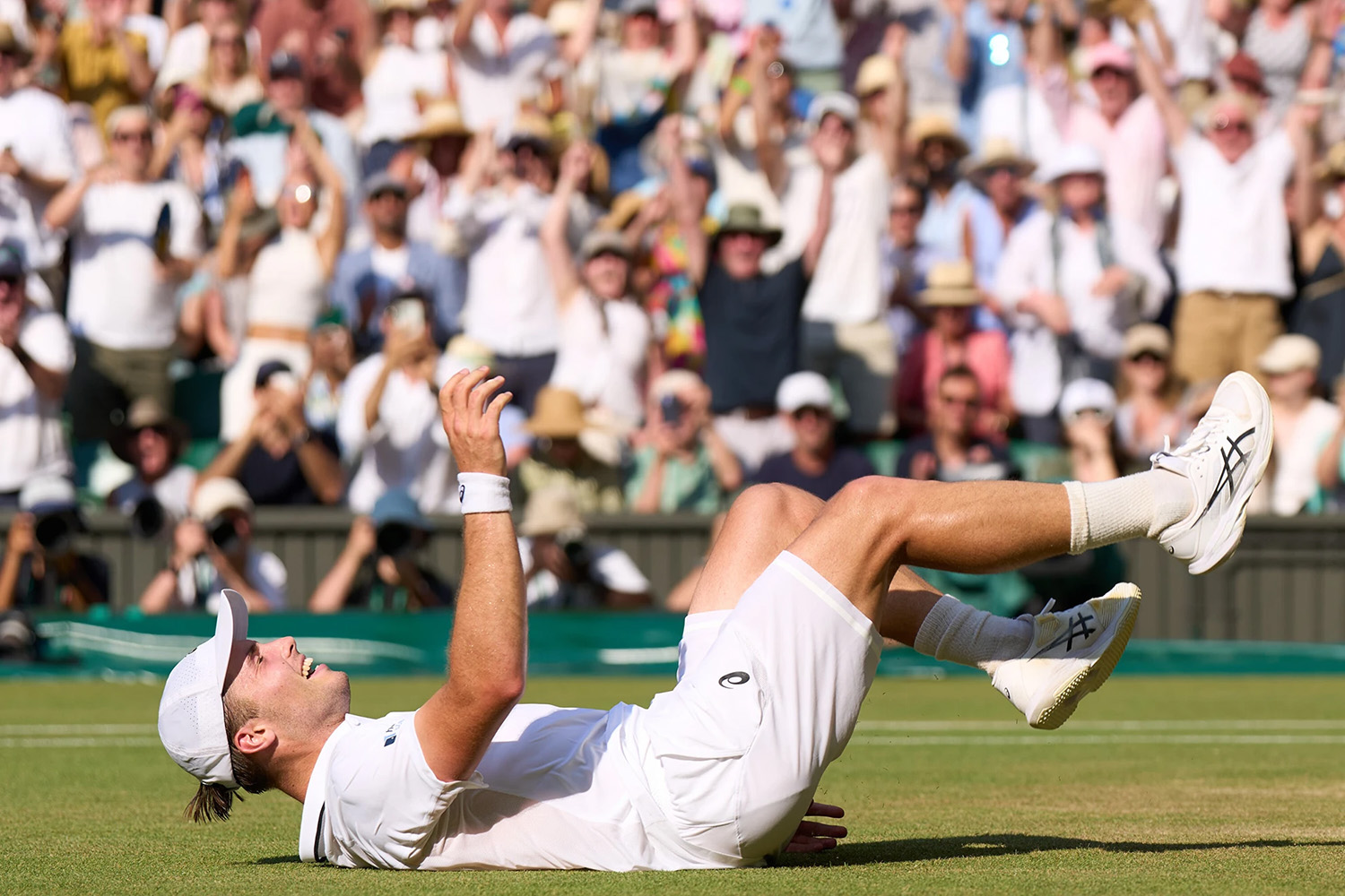 Arthur Fery falls onto his back on the grass court in celebration as the Wimbledon crowd cheers behind him.