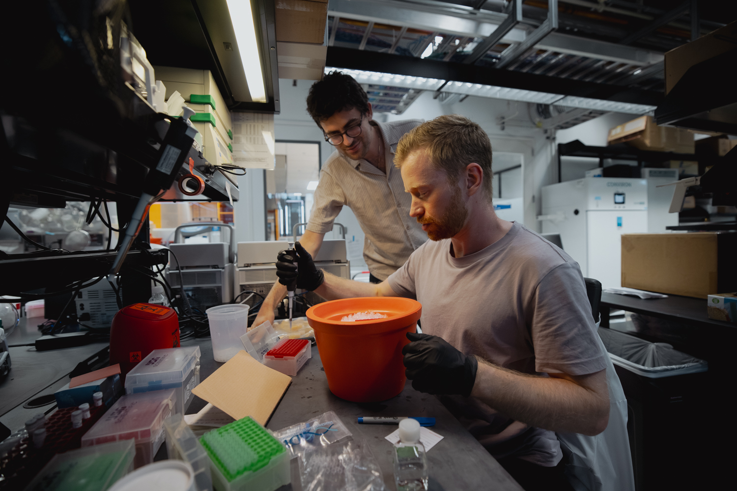 Vayu Hill-Maini watching over another researcher at a lab bench pipette samples.