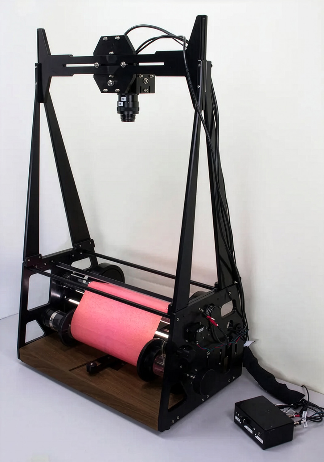 A custom-built scanning rig holds a pink piano roll beneath an overhead camera, used to digitize the roll's punched patterns.