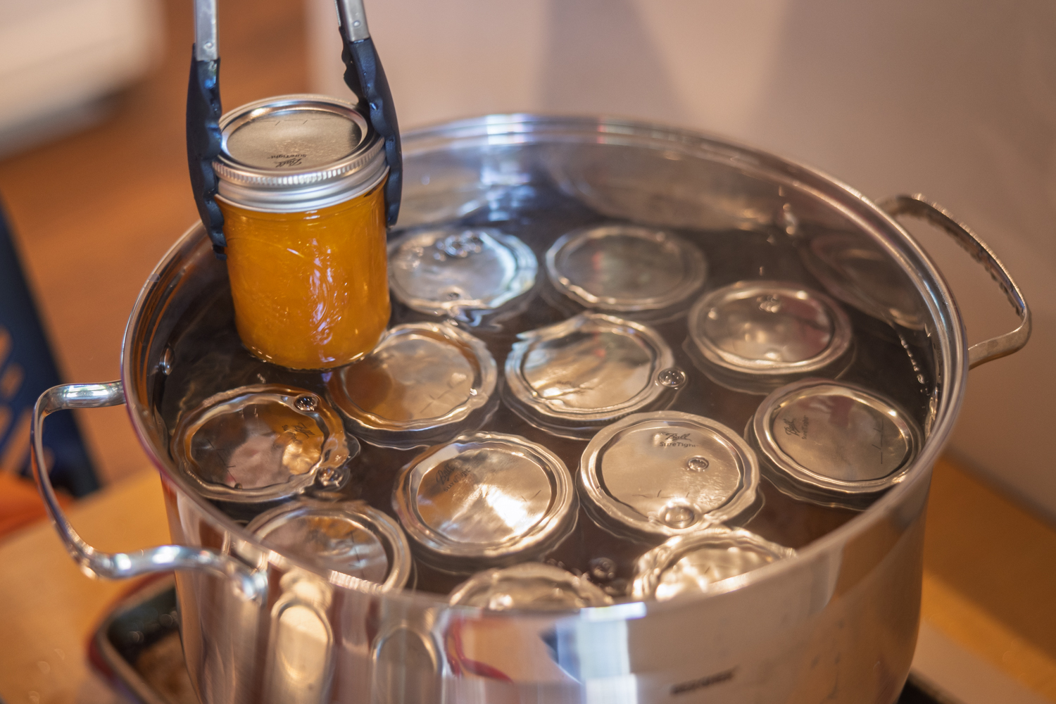 Jar of apricot jam being lifted from a boiling water bath canner with tongs.