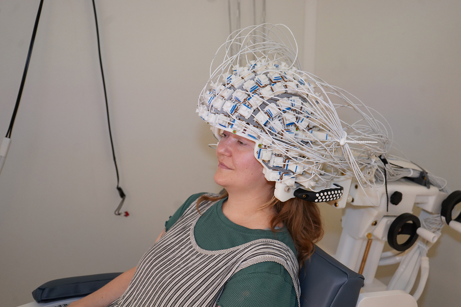 A study participant wears a dense wired sensor cap connected to brain-imaging equipment.