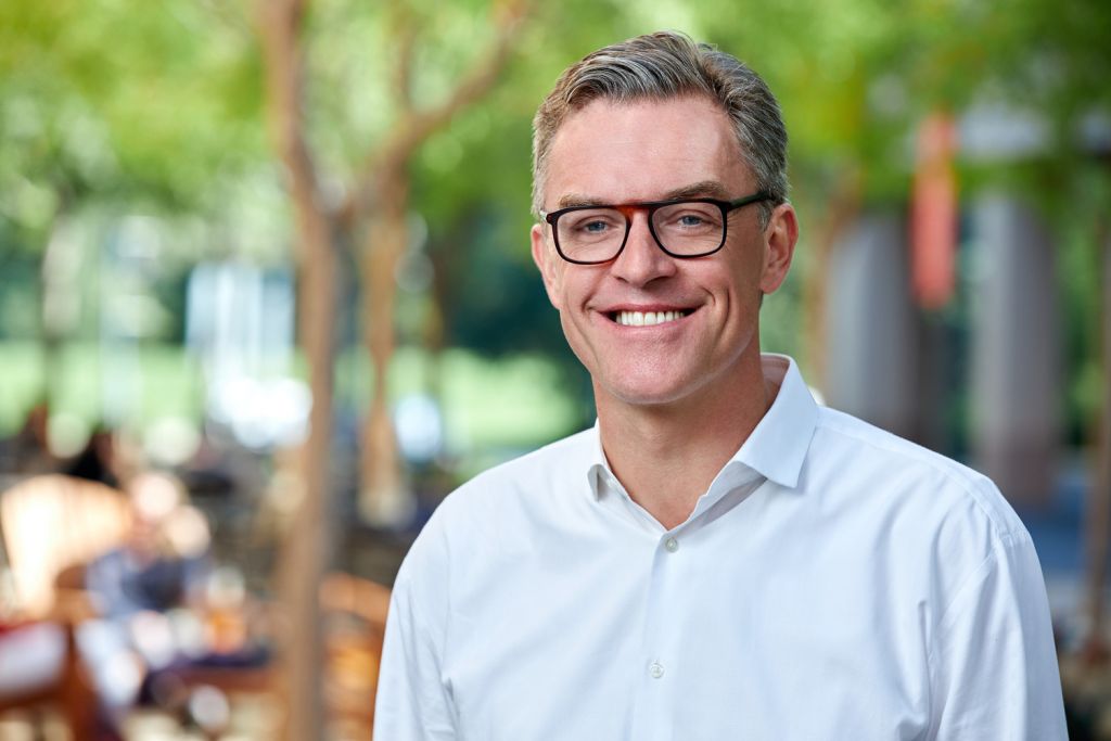 Hanno Lustig smiles for a professional headshot outdoors, wearing glasses and a button-down shirt.