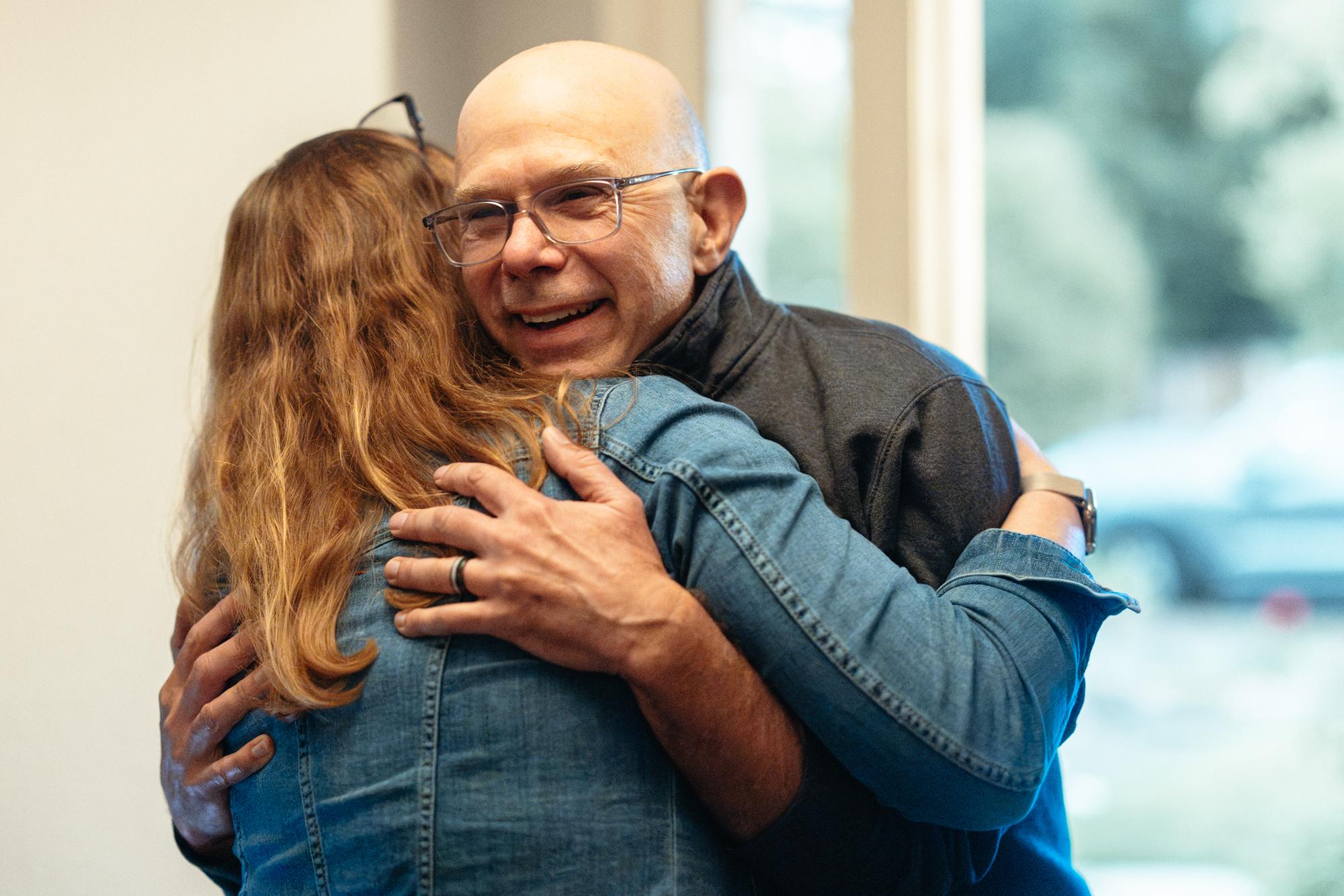 Michelle Monje-Deisseroth with long auburn hair and a denim jacket and Scott Delp, with bald head and glasses, embrace.