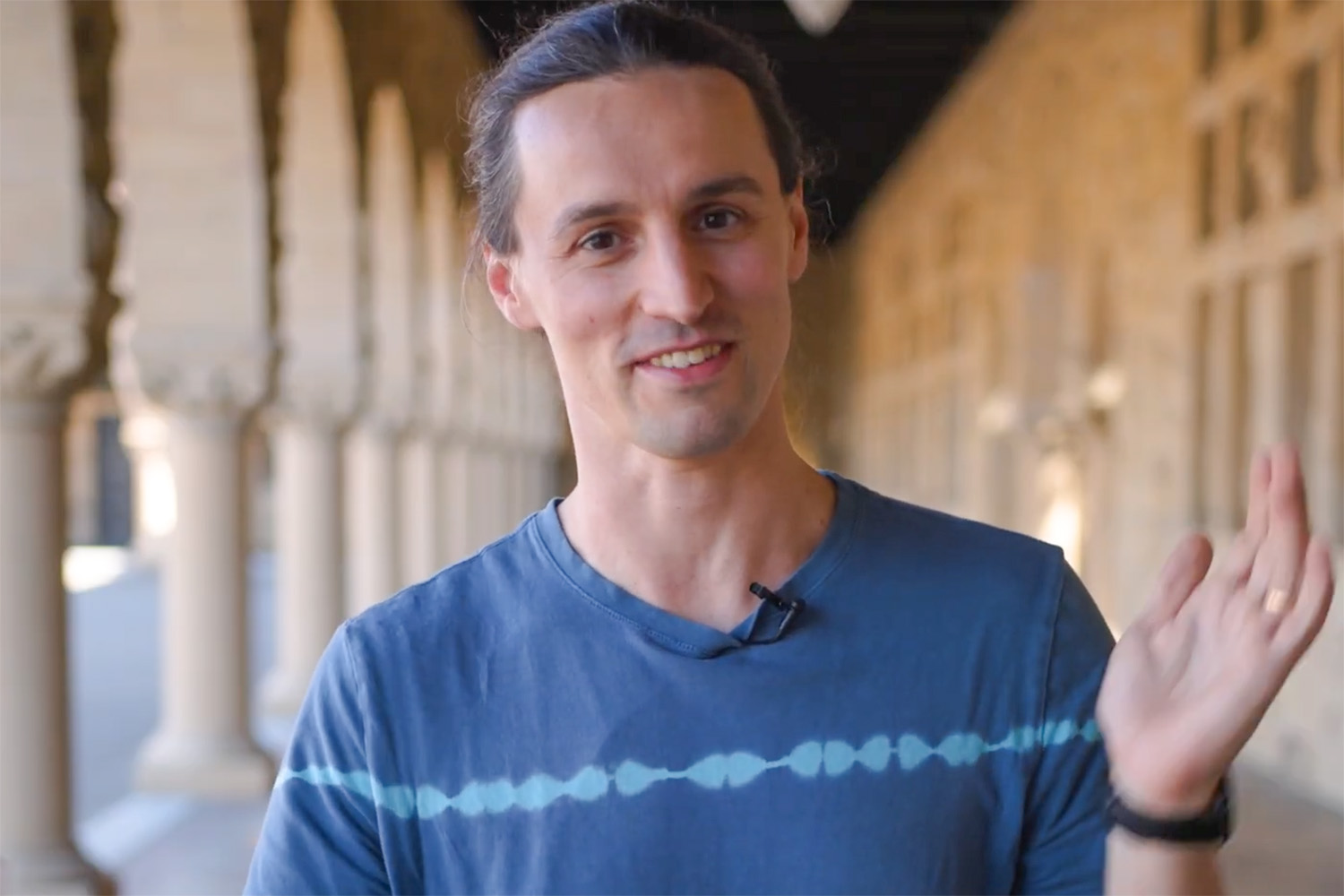 Open video Ettore Biondi, wearing a clip-on microphone, waves gestures with his hands while talking in a sunlit sandstone arcade. in a modal