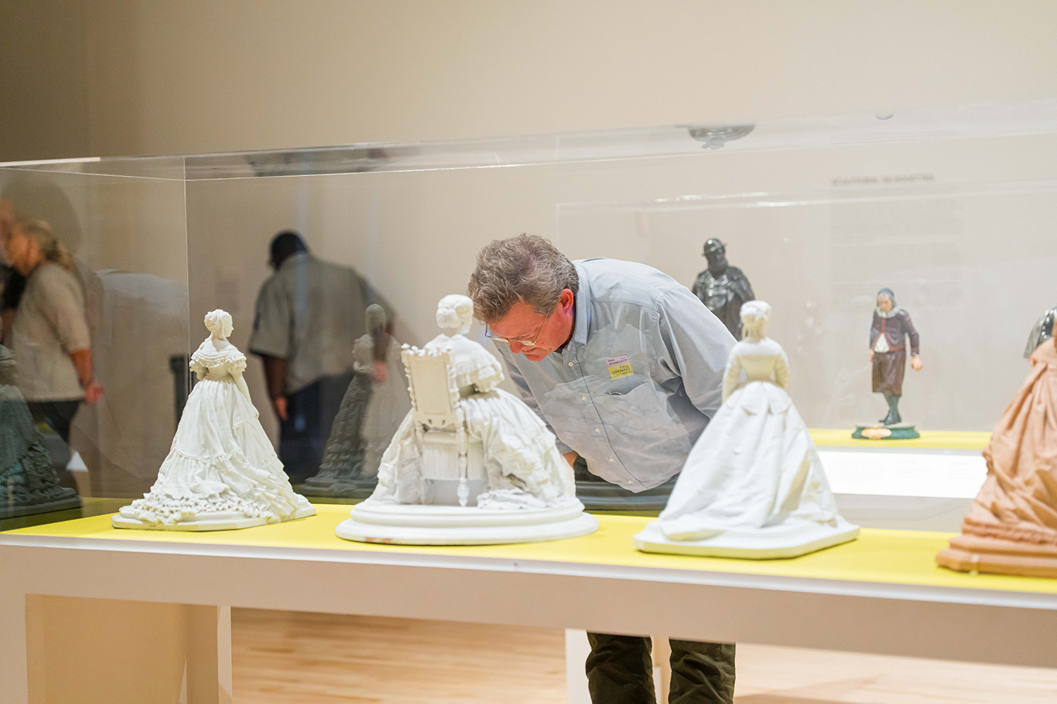 Visitor leans over a display case to examine white porcelain figurines of women in historic dress.