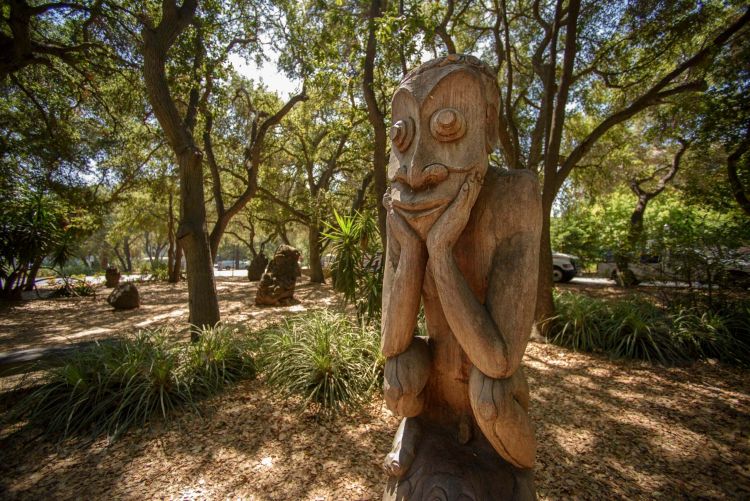 Carved in wood, The Thinker (Yerakdu) in the Papua New Guinea Sculpture Garden depicts the story of an ancestor sitting alongside the hole from which he emerged into the world. He is thinking about how he can create fellow humans out of clay. His first attempt has just failed, and broken body parts are scattered around his feet. (Image Credit: L.A. Cicero)