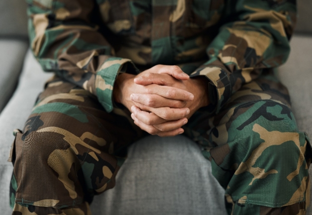 A veteran in army fatigues clasps their hands together.