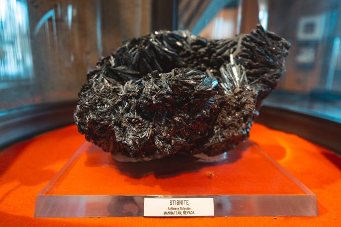 A black mineral on display with a plaque that reads "stibnite, antimony sulphide, Manhattan, Vietnam" (Image Credit: Andrew Brodhead)