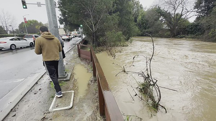Pictured is a man standing next to temporary floodwall that's holding back rising water in East Palo Alto.