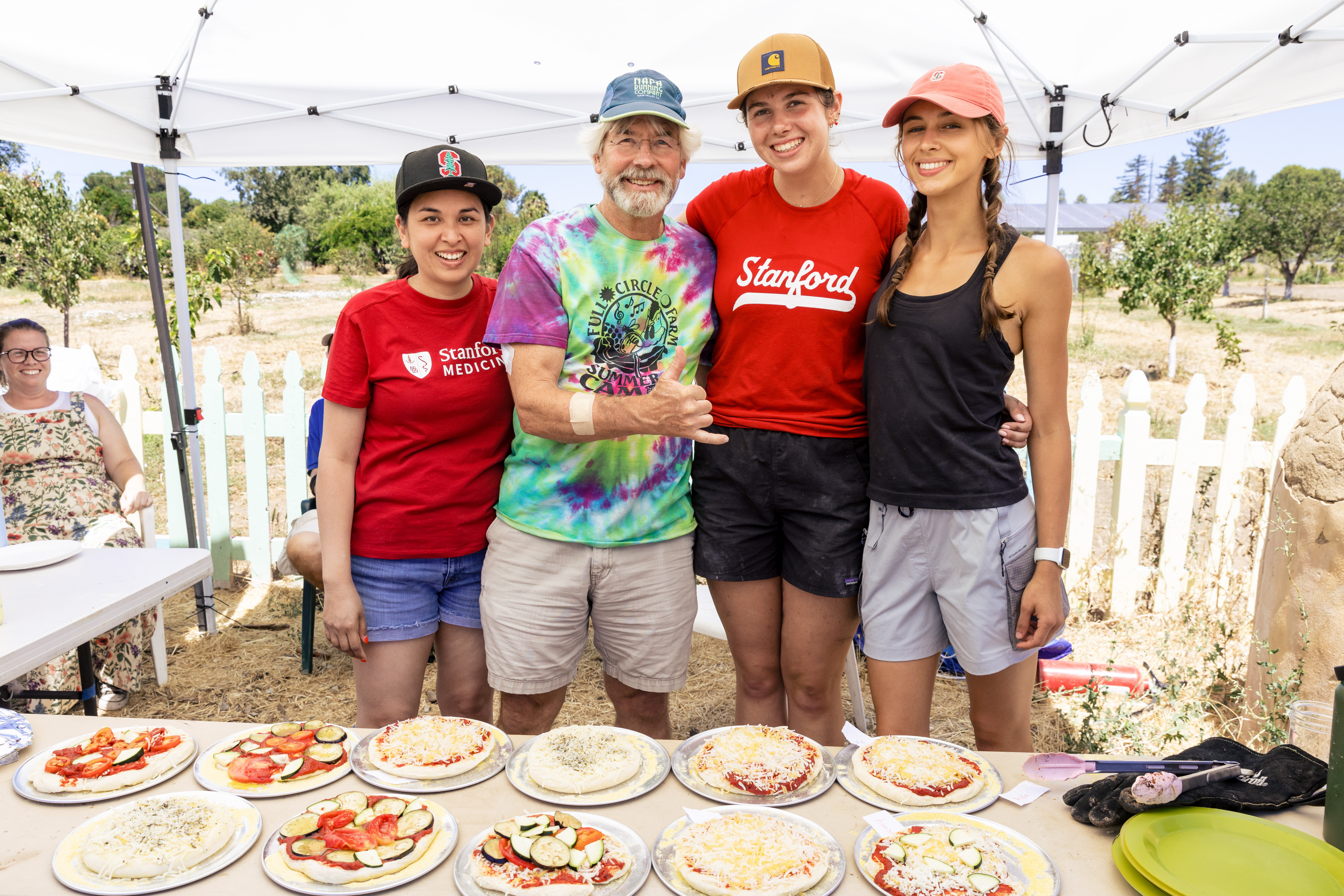 Camp leaders stand under a tent behind a table laden with assembled pizzas waiting to go into the oven.