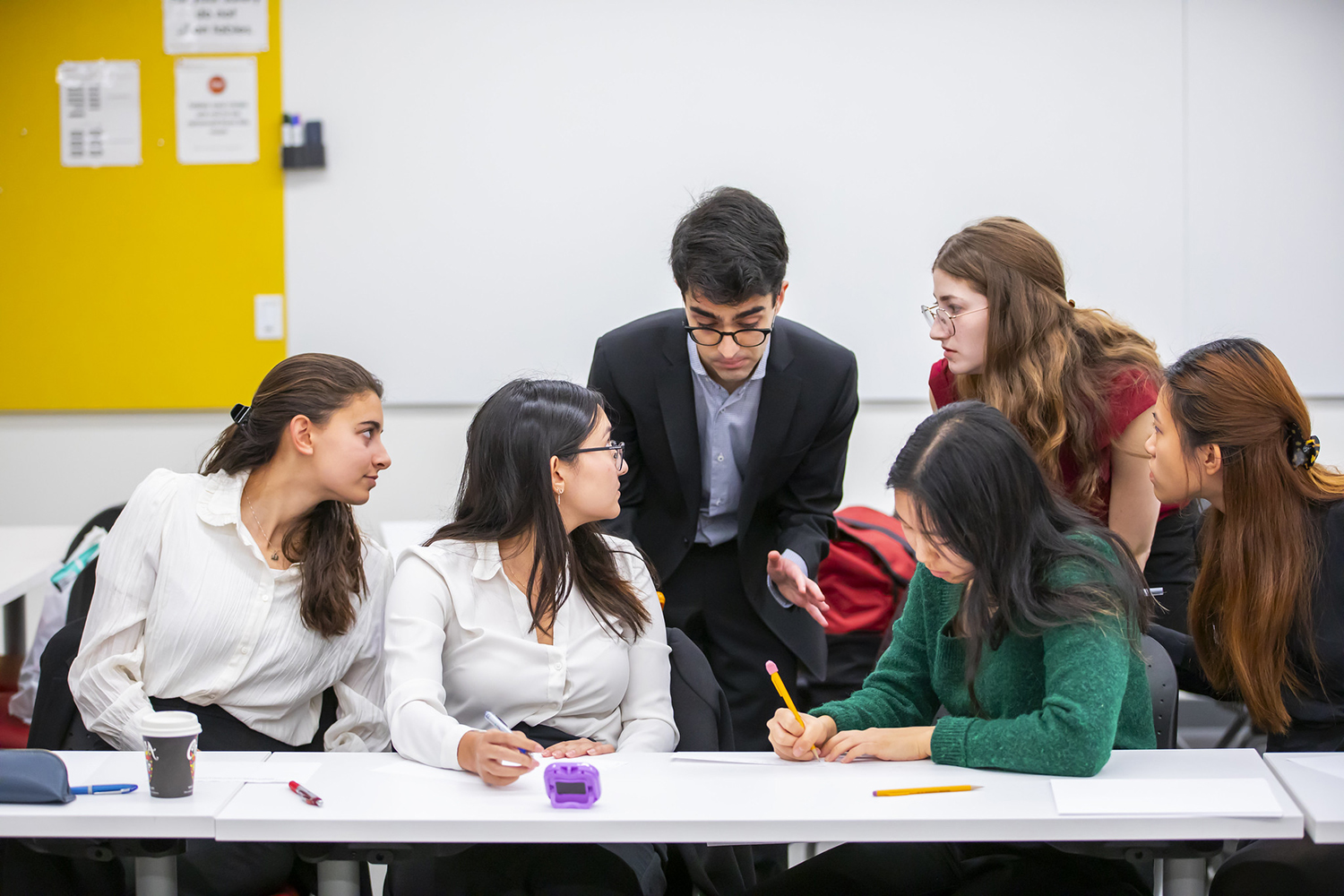 Image of Stanford students huddled together at a table to discuss their speaking points.