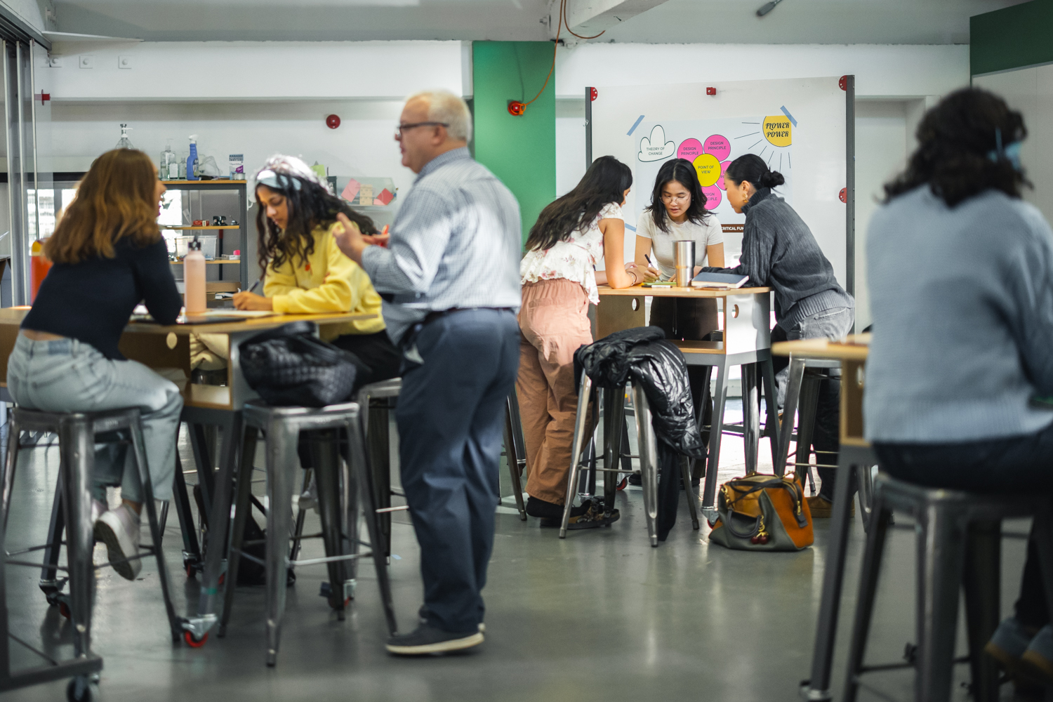 A wide shot of students in a classroom, sitting on high-top chairs, and learning how an 11-step design process can be applied to real-world problems.