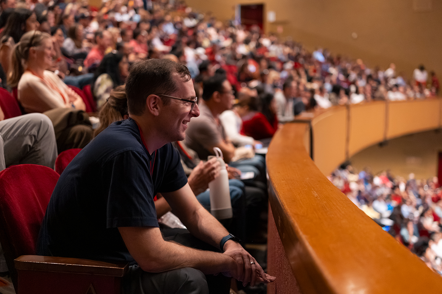 An audience member sits attentively in a theater filled with spectators, watching a presentation from the front row.