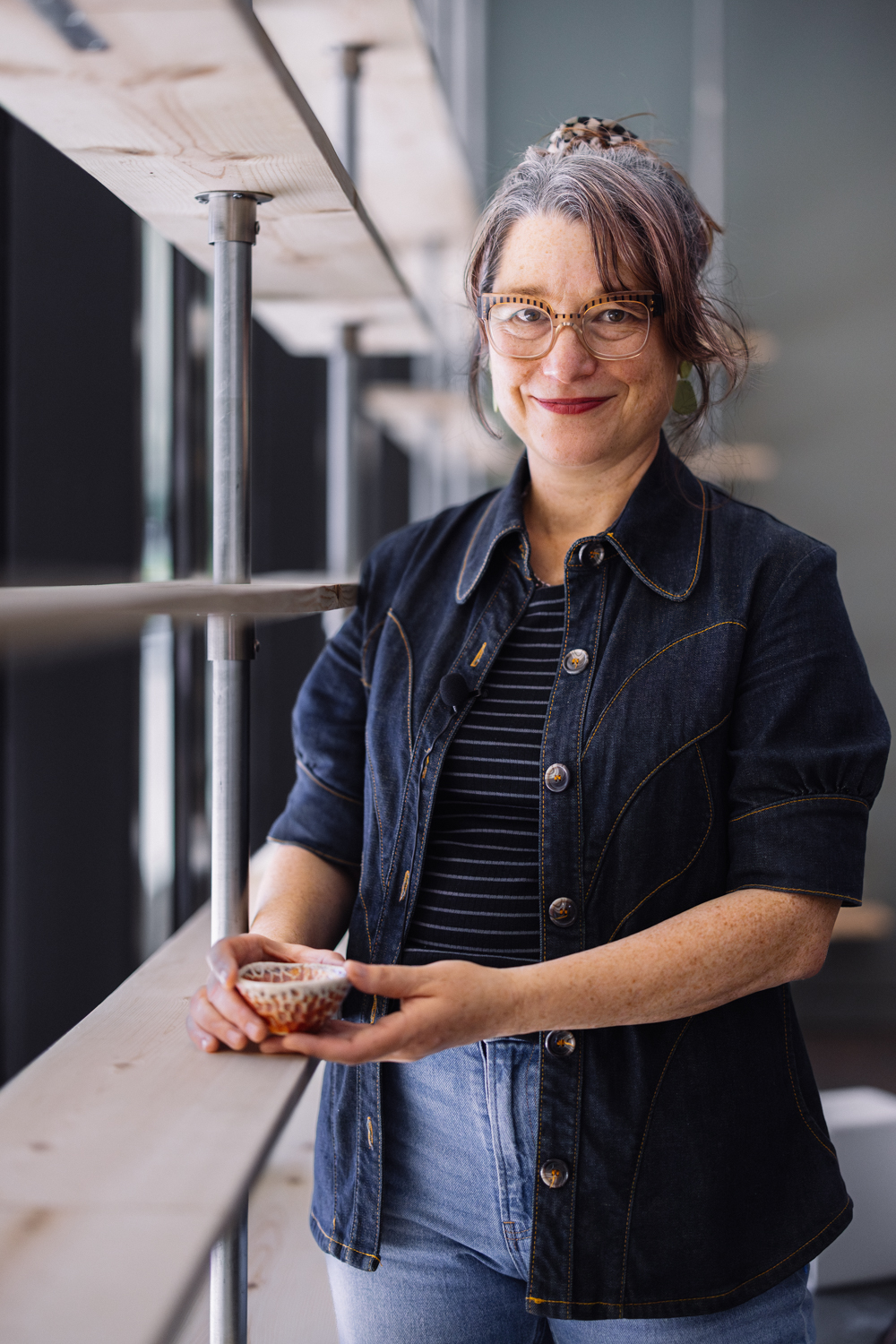 Artist holds a handmade ceramic bowl while standing in a studio workspace.