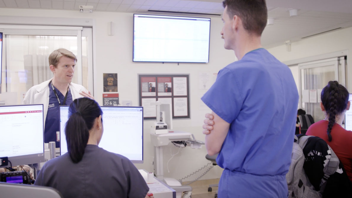 Healthcare professionals in discussion in a hospital setting with computers and screens.