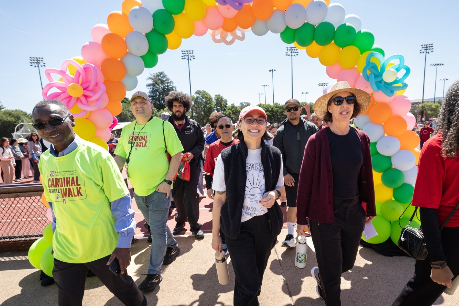 Participants walking through a colorful balloon arch at a community wellness event, showing excitement and camaraderie as they start the event.