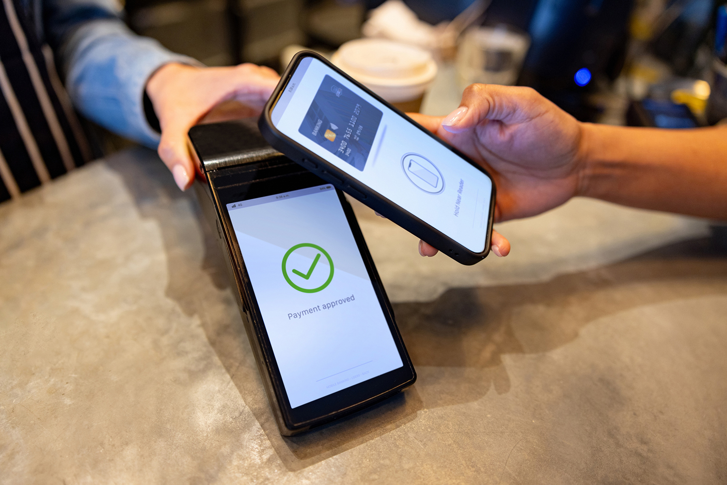 A person uses a smartphone to make a contactless payment at a register, showing a 