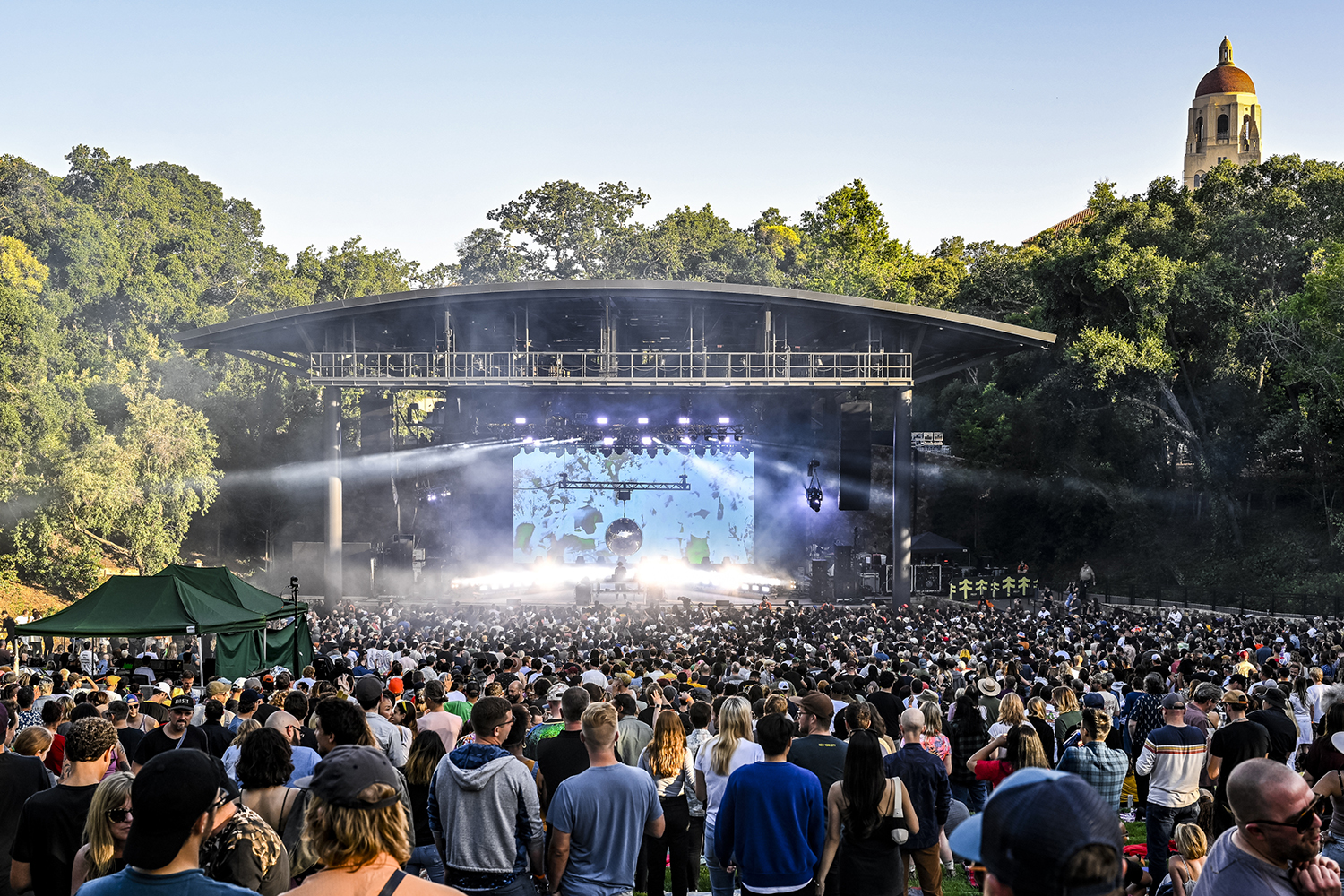 Large crowd enjoying an Atmosphere concert at Frost, with a stage displaying lights and visuals surrounded by trees. 