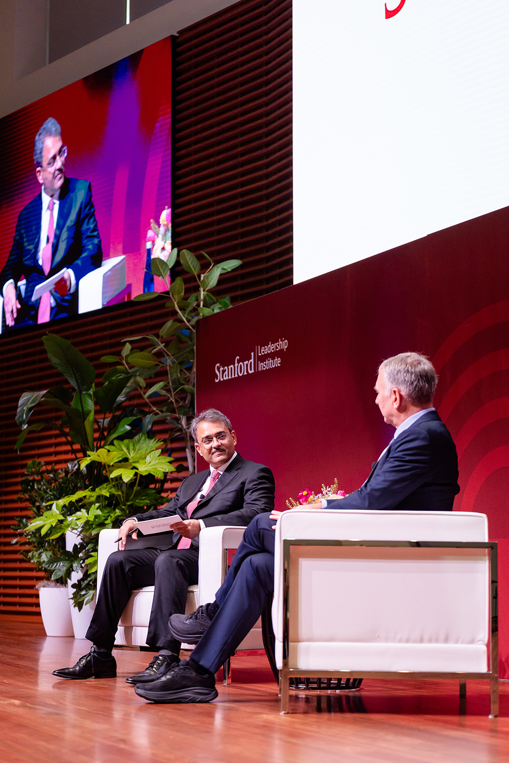 Two speakers discuss an topic at the Stanford Leadership Institute, with a large screen displaying their images behind them.