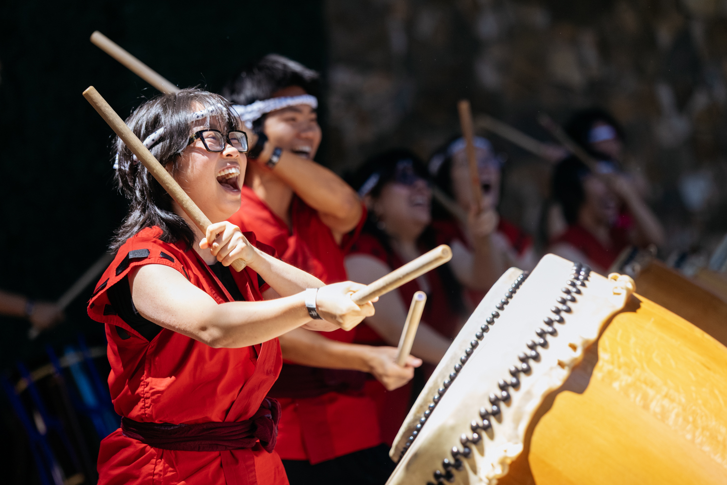 A group of performers in red outfits plays traditional drums, using wooden sticks, during Baccalaureate.