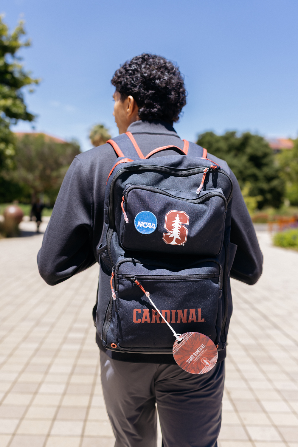 Samir Banerjee walks across campus wearing a Cardinal backpack with NCAA and Stanford logo patches.
