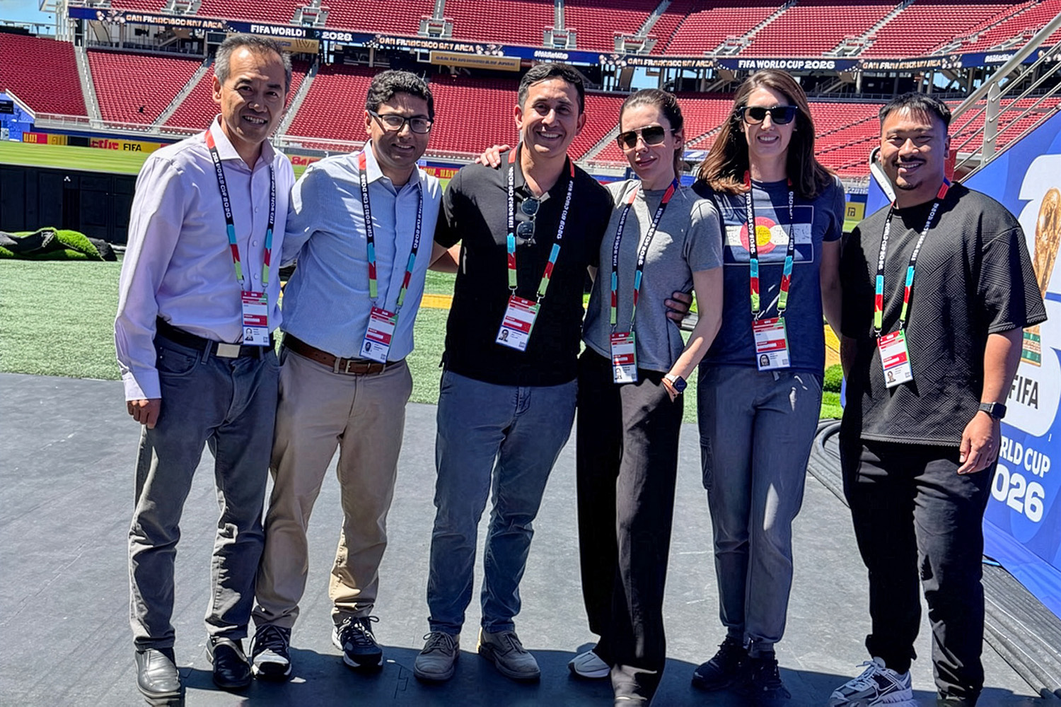 Six member of the Stanford Medicine team stand arm in arm on a stadium stage with red seats behind them.