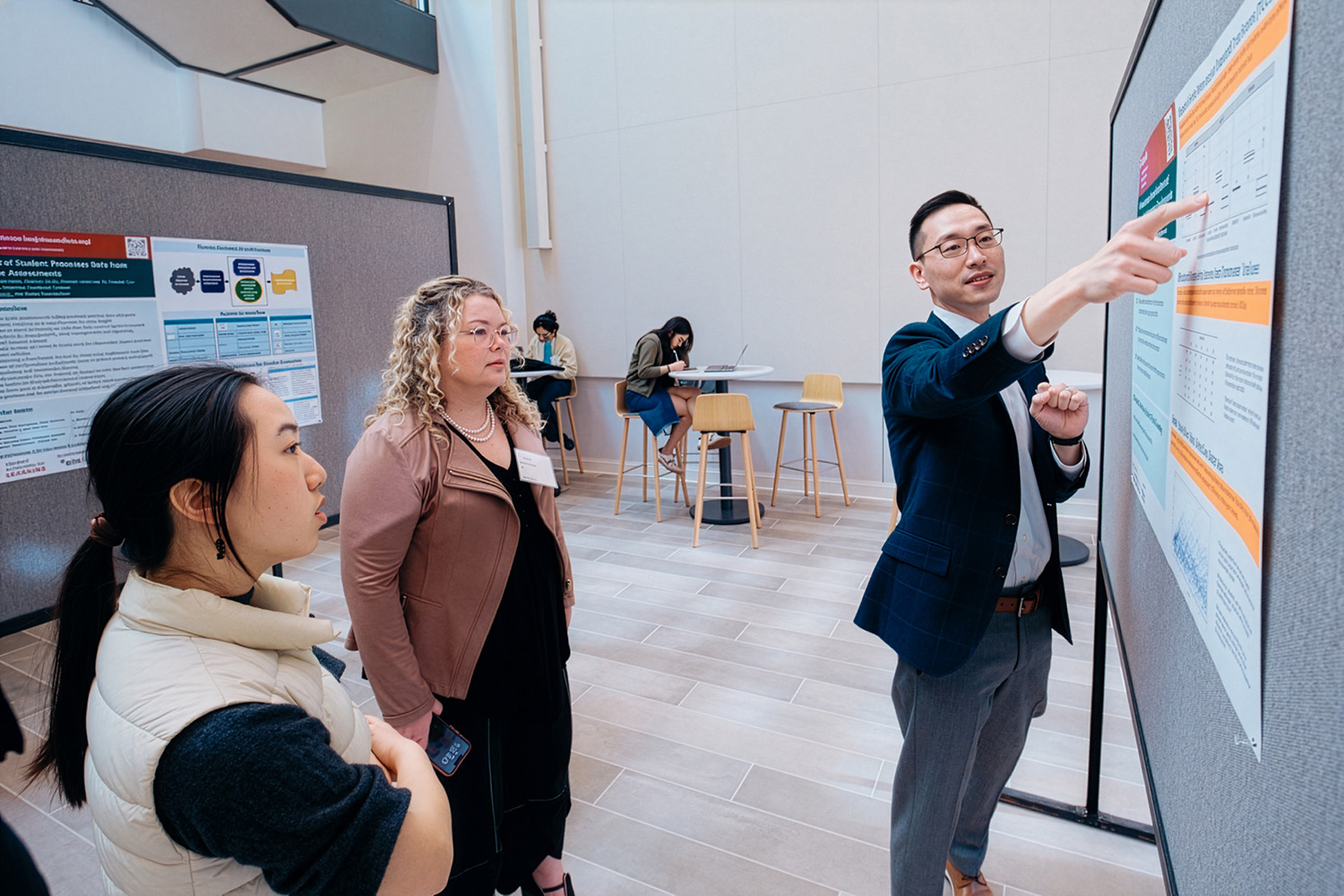A presenter discusses a research poster while two audience members listen attentively in a conference setting.