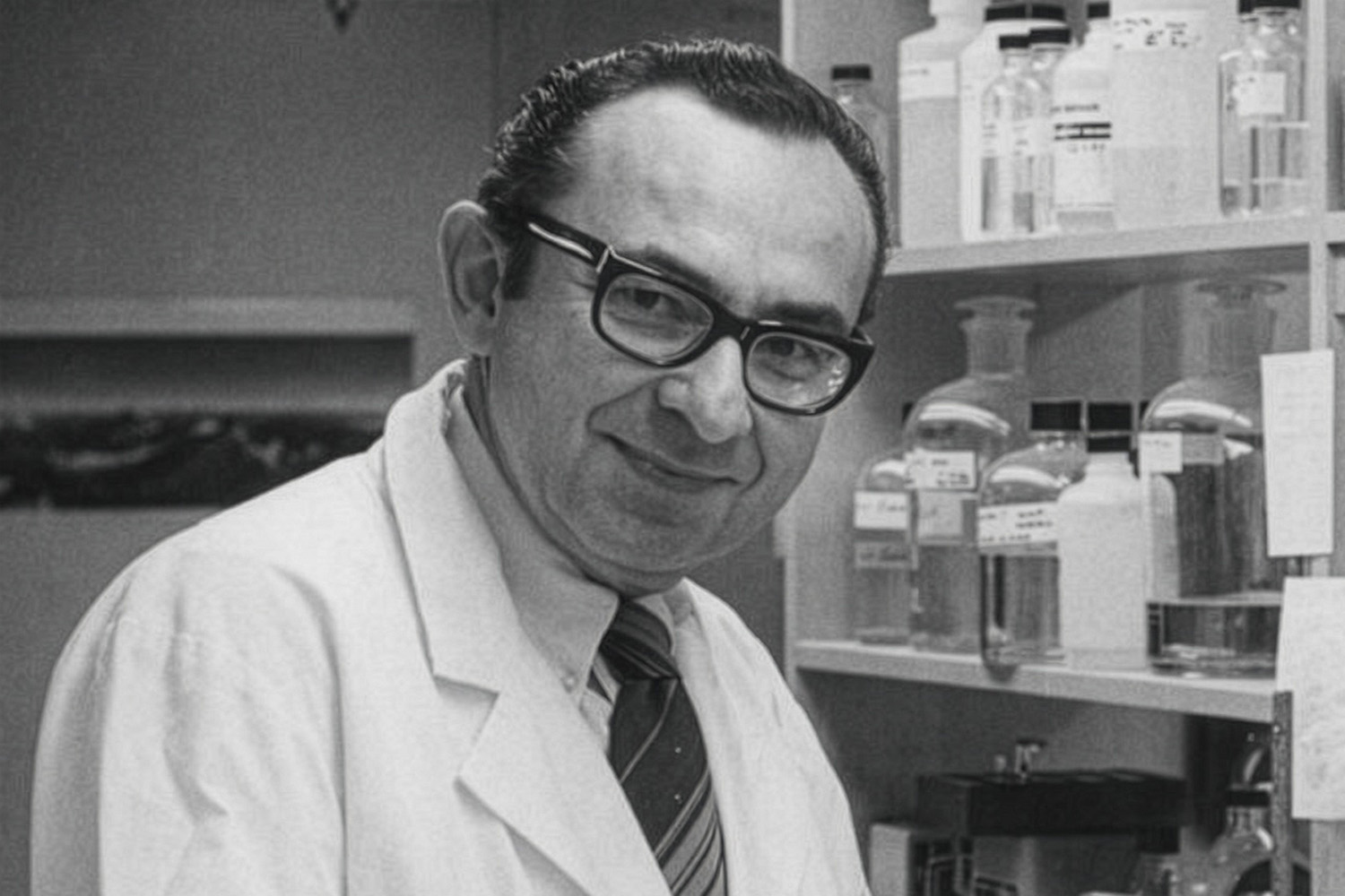 Robert Lehman, wearing a white lab coat with a dress shit and tie, poses for photo in his lab.