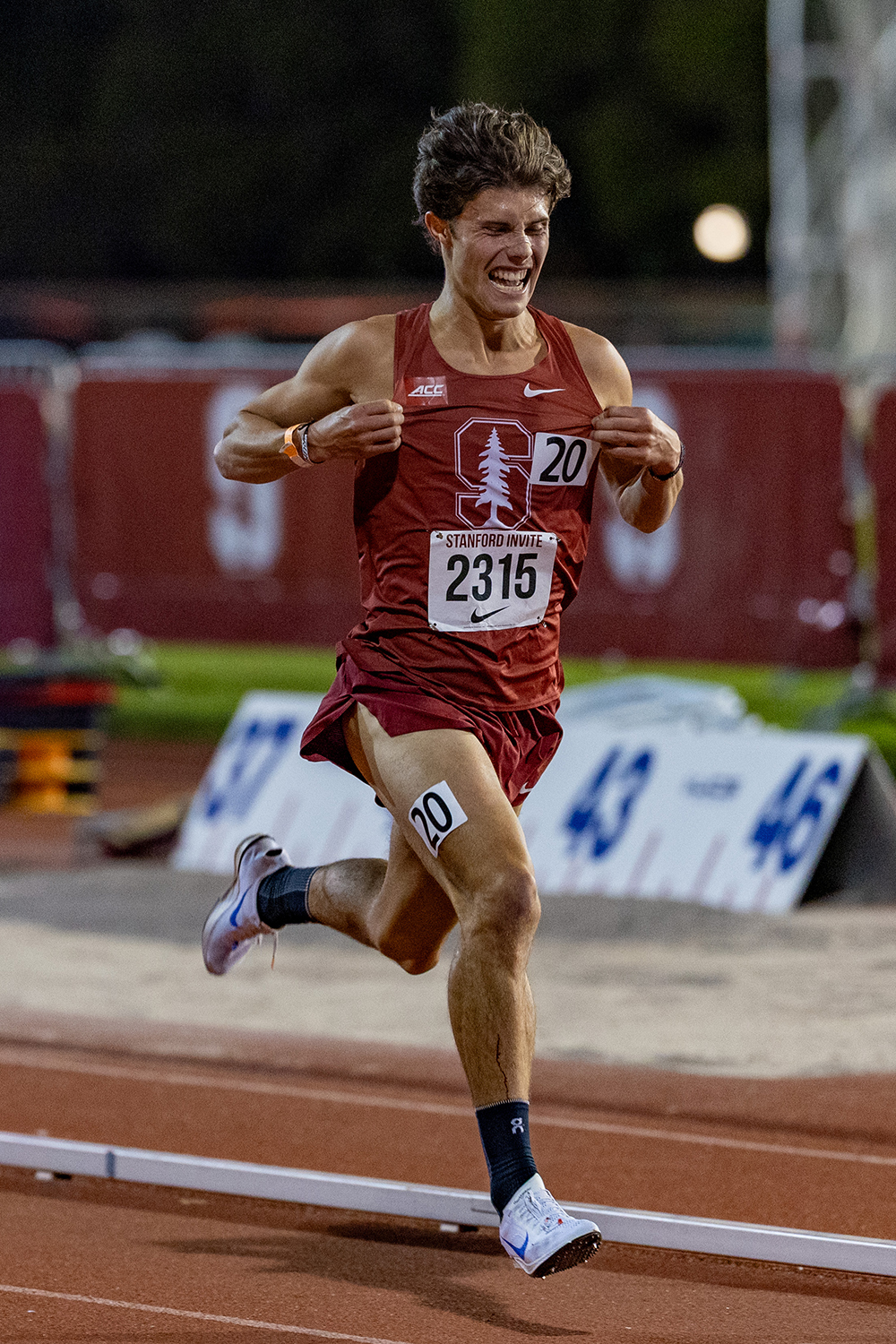 A Cardinal runner grips the front of his jersey while striding along a track.